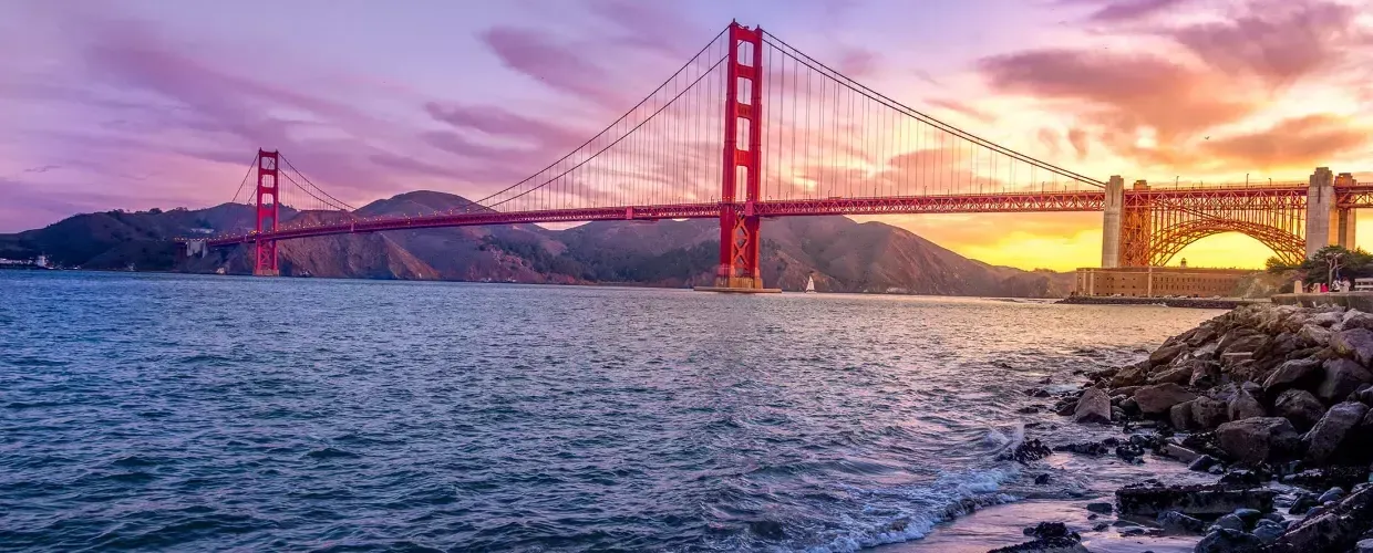 El puente Golden Gate al atardecer con un cielo multicolor y la Bahía de San Francisco en primer plano.